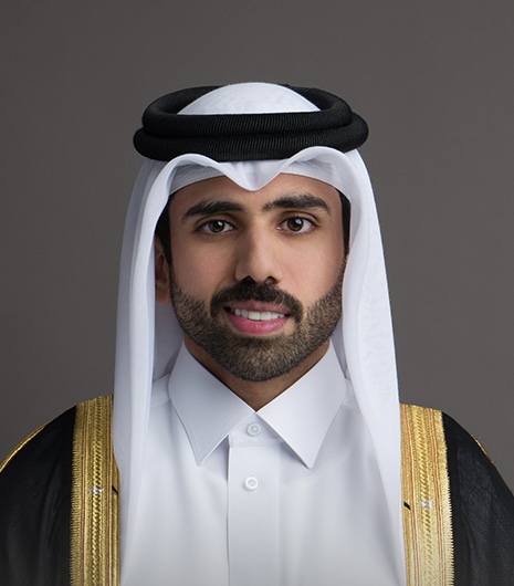 Formal bisht portrait of a Qatari man in a gold trimmed black bisht over a white thobe, photographed on a grey studio backdrop.